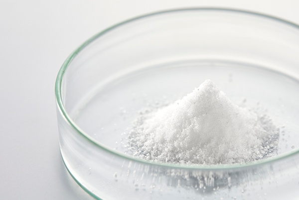 White powder in a glass dish on a light surface.