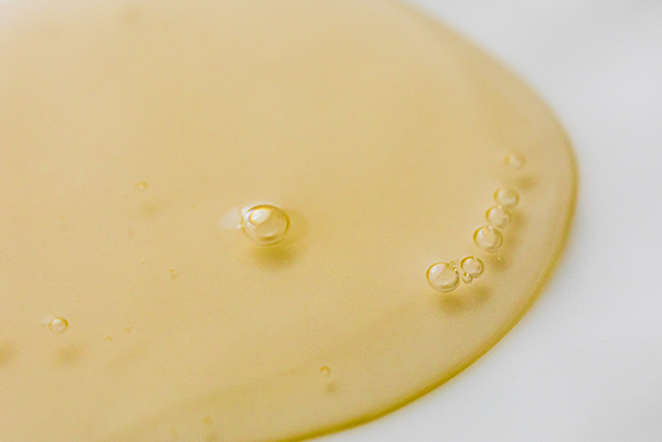 Close-up view of a golden-yellow liquid with several small bubbles on a smooth white surface, resembling castor oil.